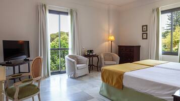 A hotel room with a bed, two chairs, a TV, a lamp, and a balcony with a view.