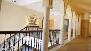 Um hall imponente com piso de mármore, colunas brancas e corrimão de madeira.