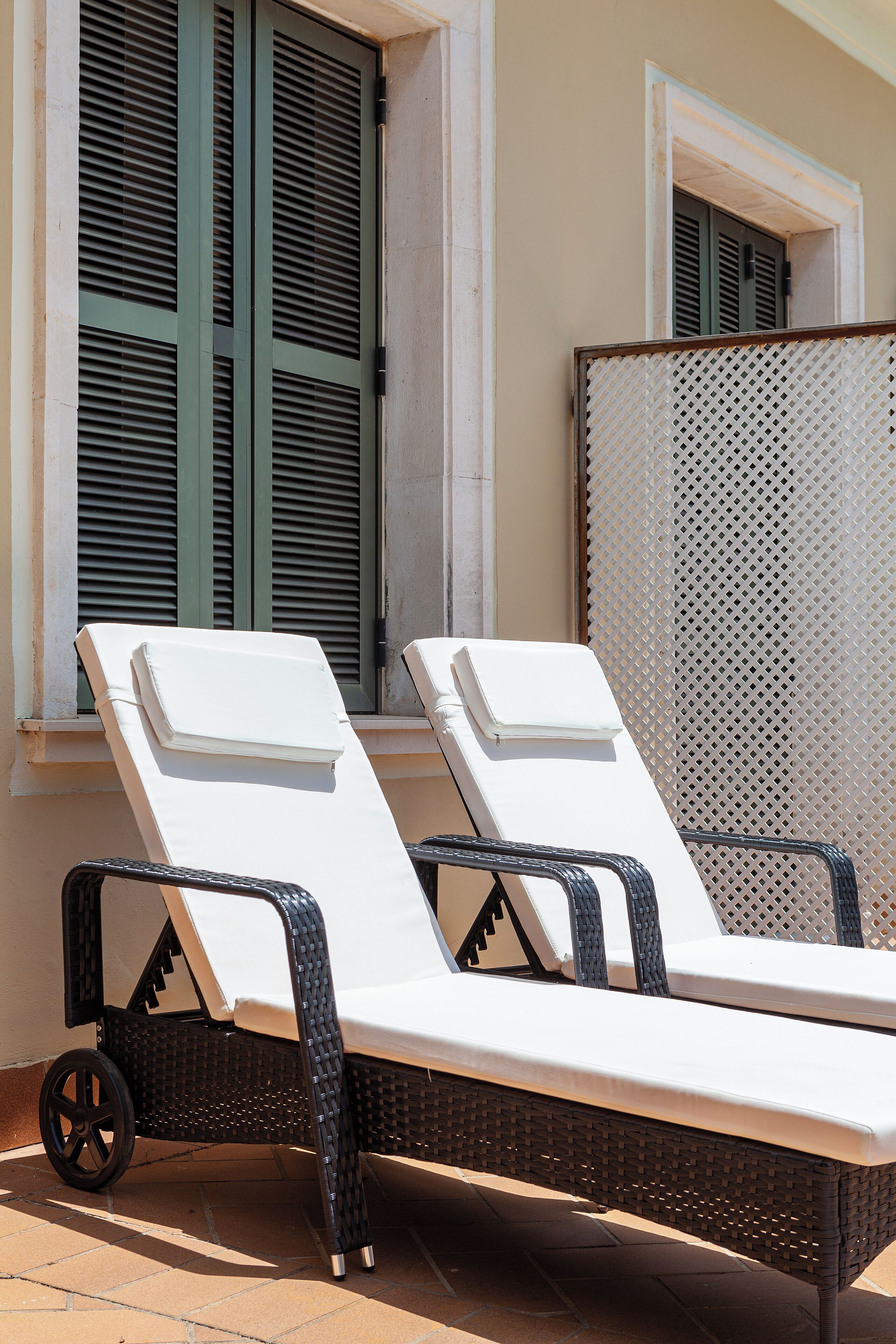 Two lounge chairs with white cushions, positioned on a tiled patio area with a wicker table and a metal chair.