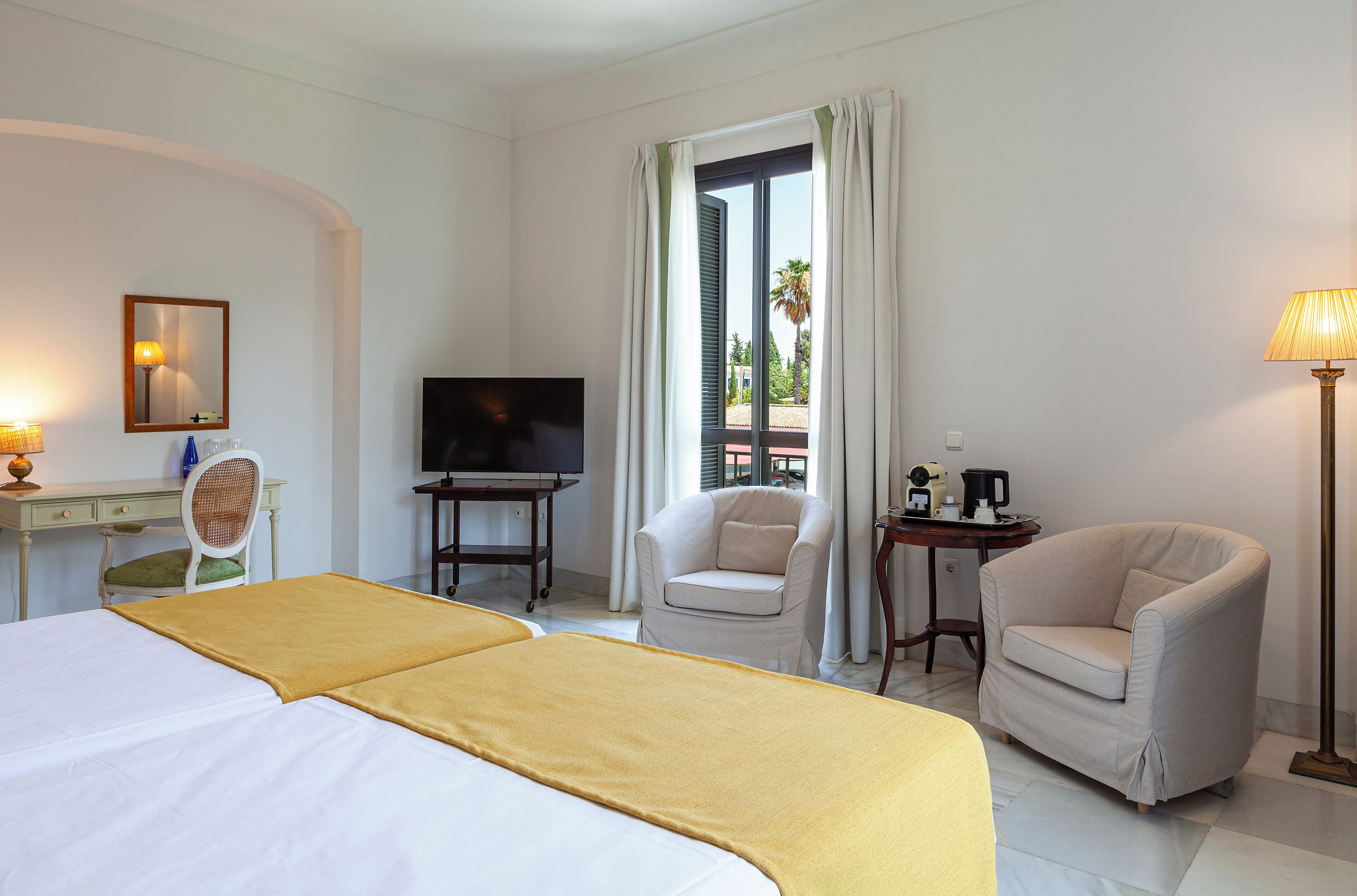 Una habitación de hotel con cama, una silla, un escritorio con televisor y una ventana con cortinas.