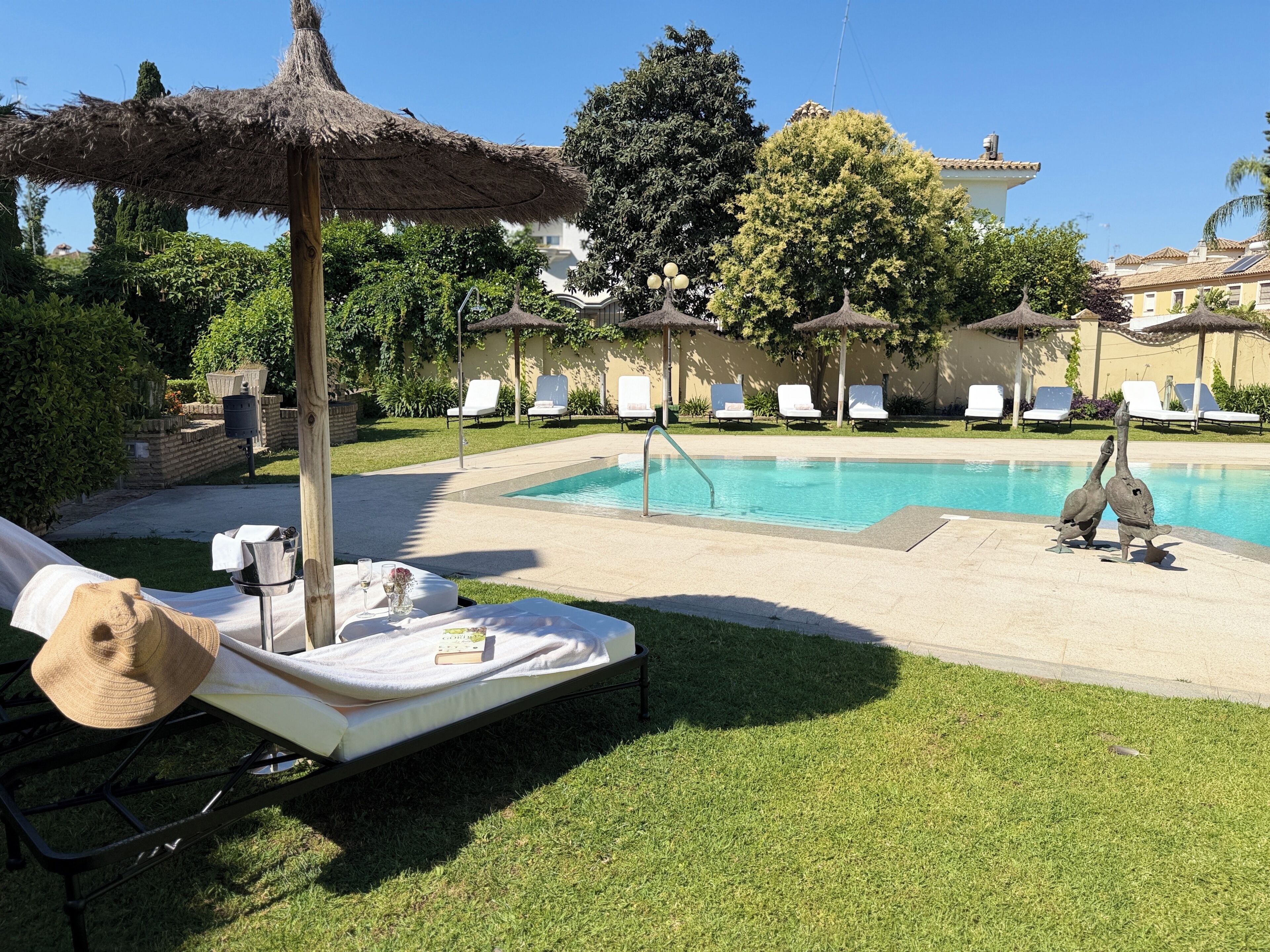 A poolside area with lounge chairs, a thatched umbrella, and a statue.