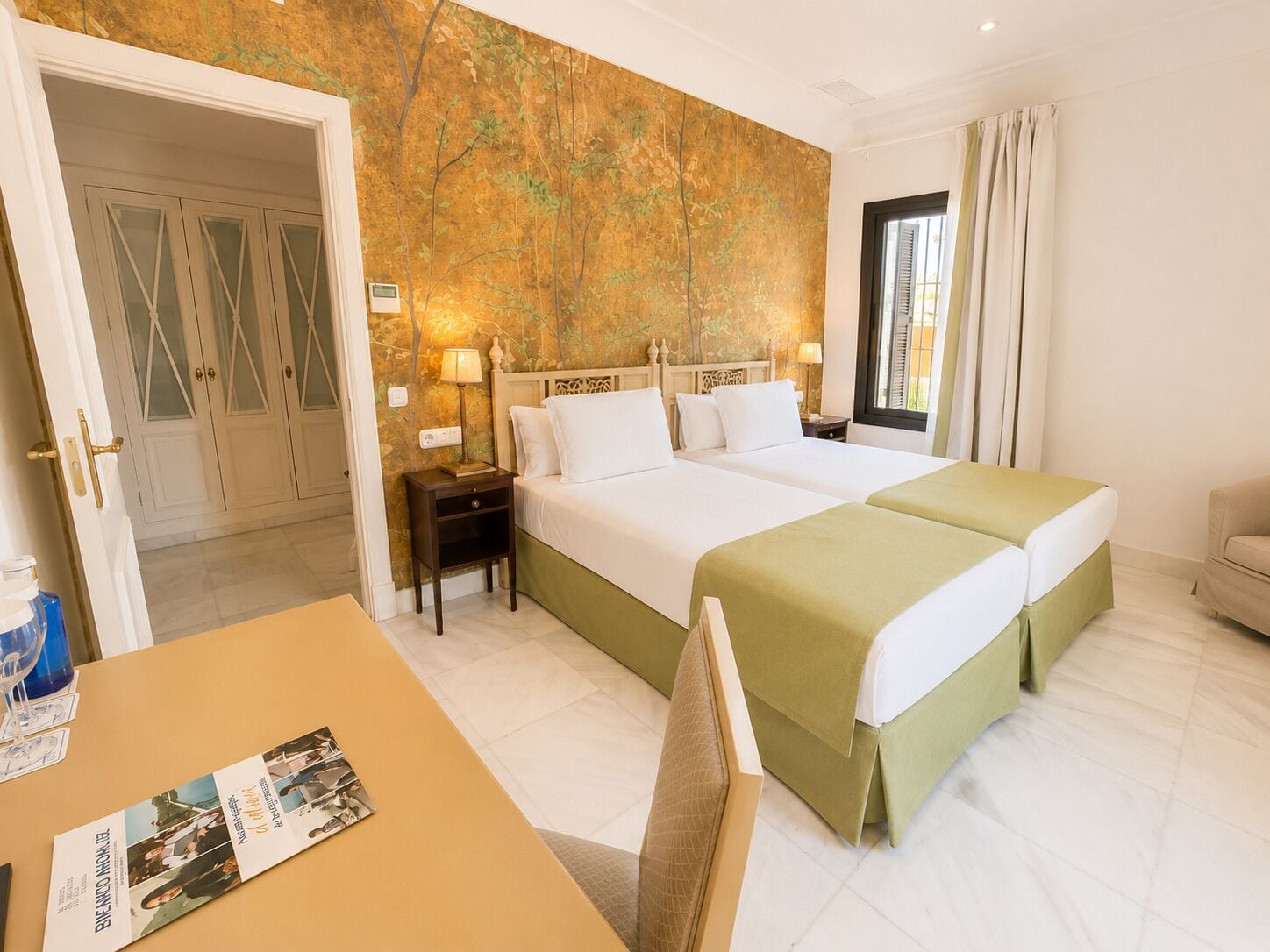 Camera d'albergo con un letto matrimoniale, un comodino, un tavolo con una rivista e vista all'esterno tramite una finestra.