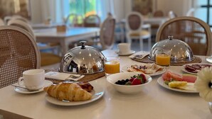 Mesa posta para dois com croissants, fruta e sumo de laranja.