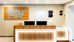 Un comptoir d’accueil avec un revêtement en bois et un tapis noir sur lequel est inscrit « MICROHOTEL BY WYNDHAM » à l’entrée.
