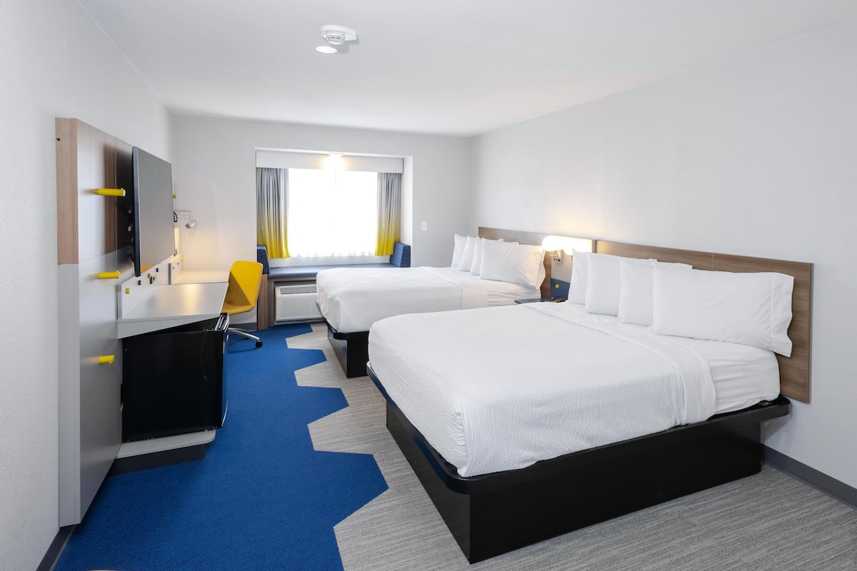 A hotel room with two beds, a desk, a chair, and a window with curtains.