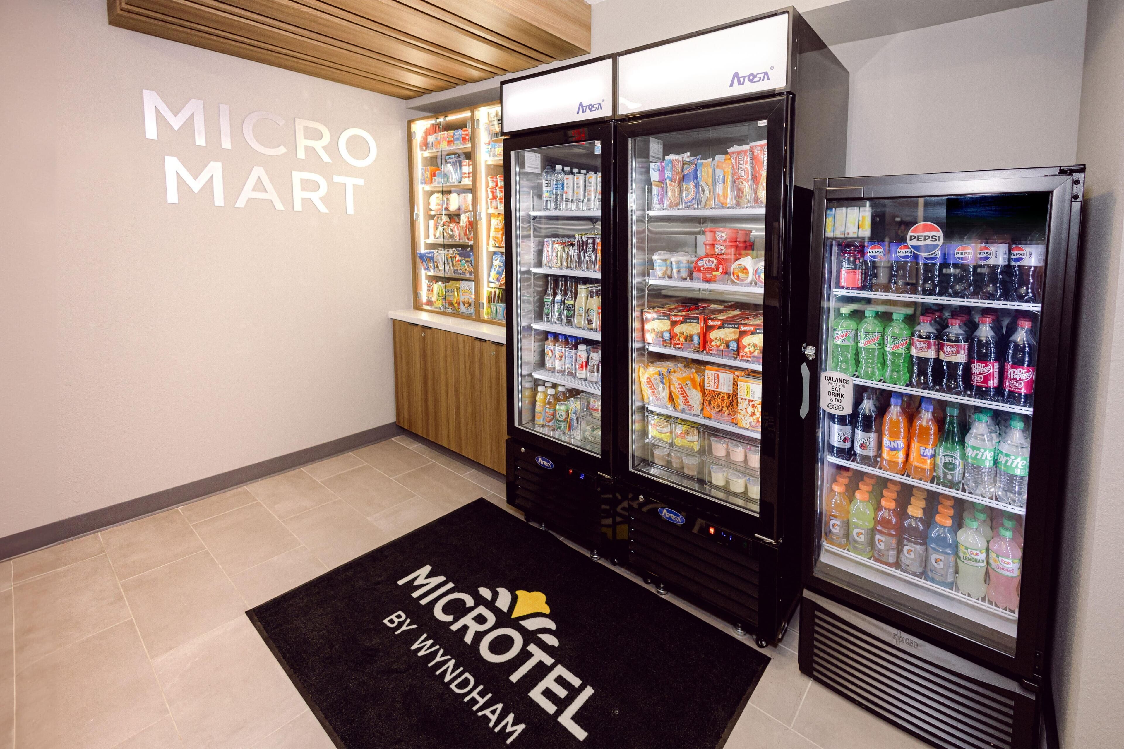 A MicroMart vending area with various beverage and snack options, a wooden ceiling, and a black floor mat with the MicroMart logo.