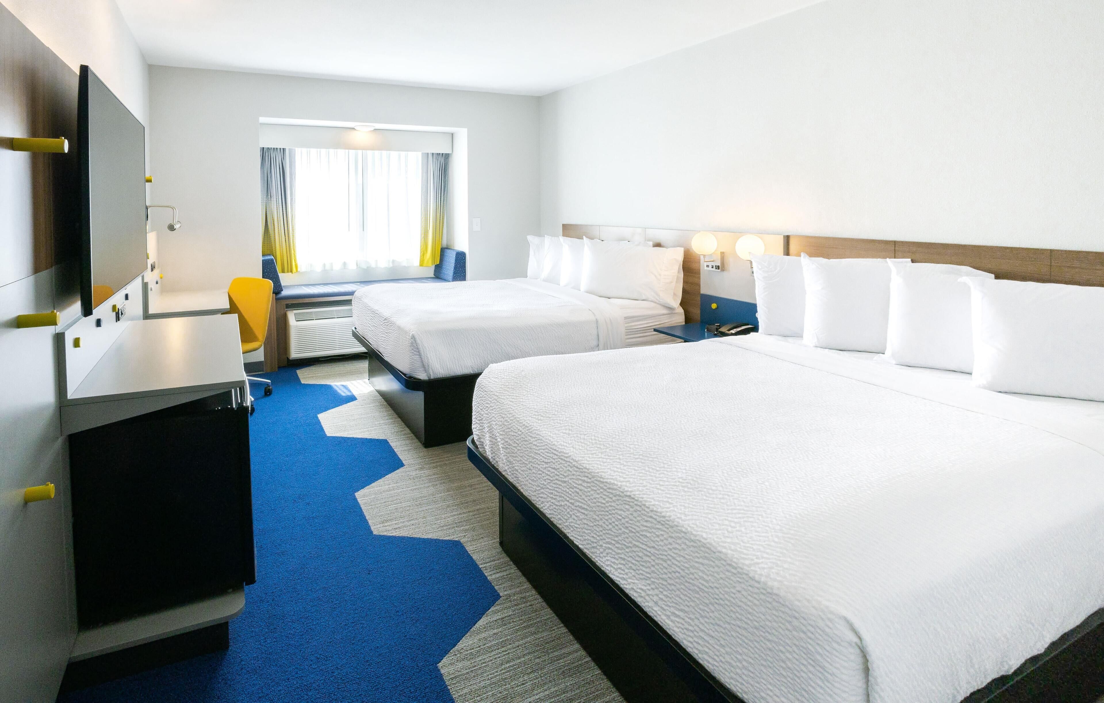 Quarto de hotel com duas camas, uma escrivaninha, uma cadeira e uma televisão.