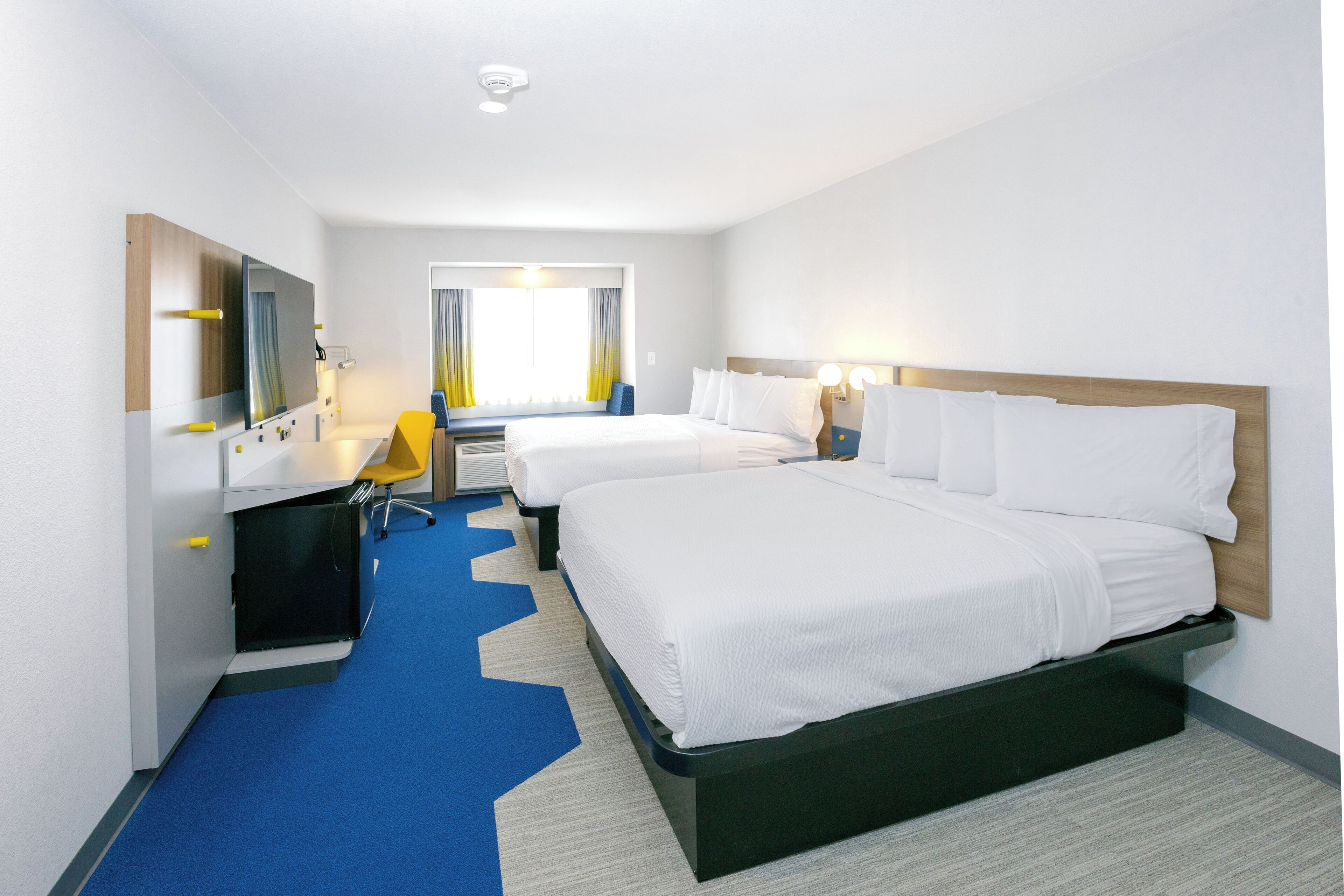 Une chambre d’hôtel avec deux lits, un bureau, une chaise, un miroir et une fenêtre avec des rideaux.