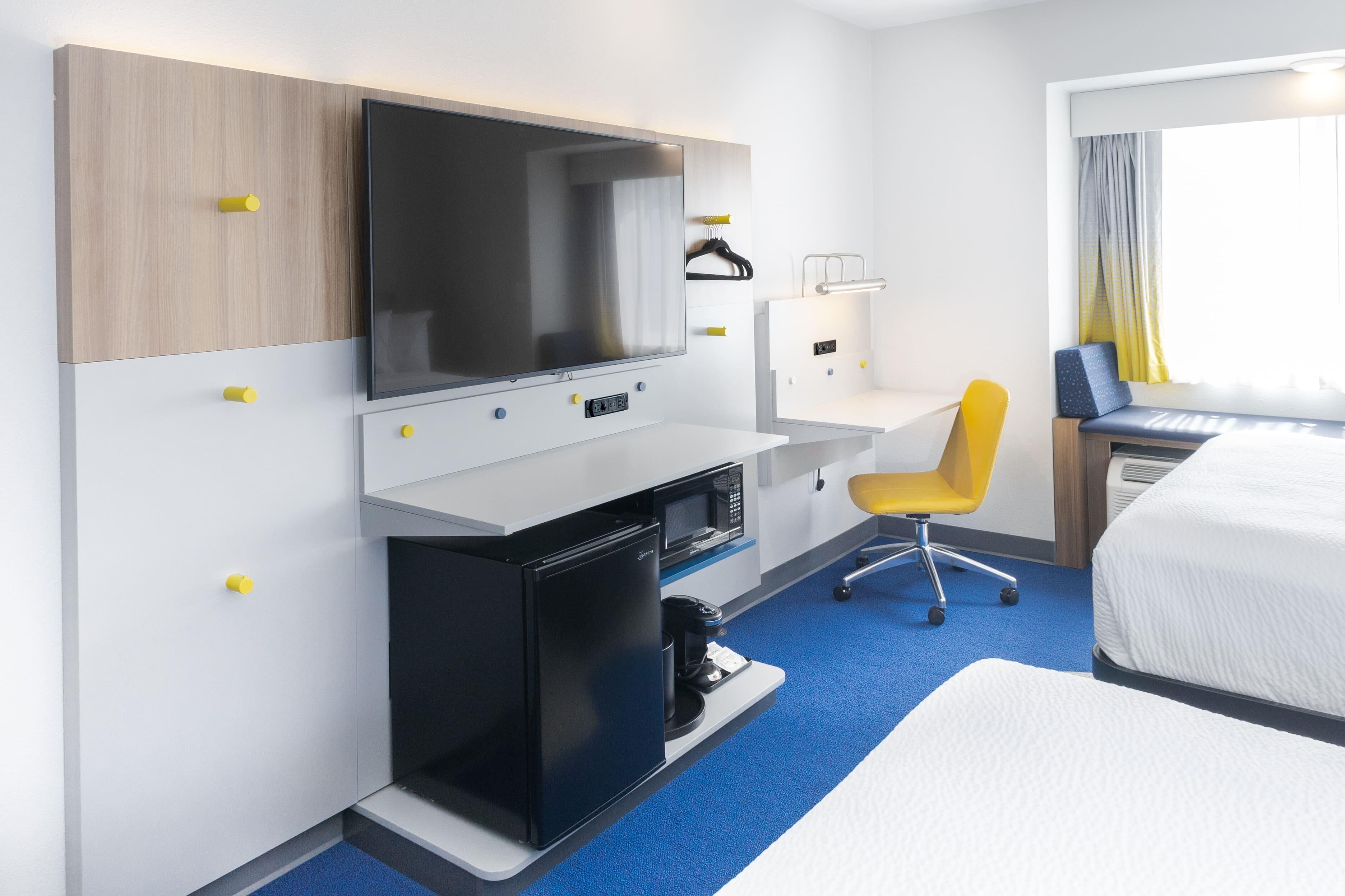 A hotel room with a bed, a desk with a computer, a TV, a microwave, and a chair.