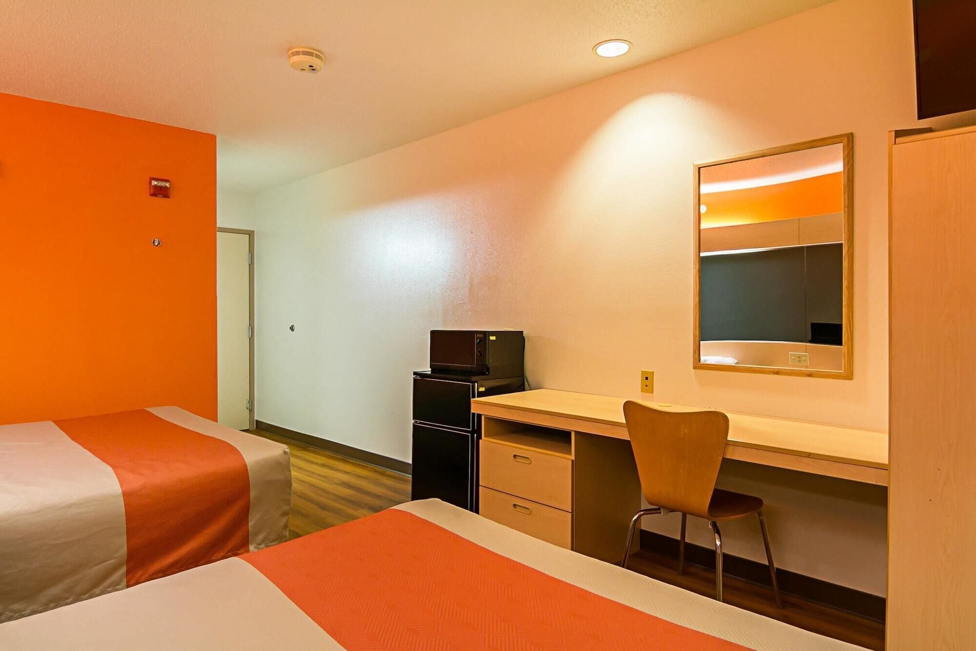 A hotel room with two beds, a desk, a chair, a microwave, and a mirror.