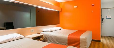 A hotel room with two beds, a large mirror, and orange walls.