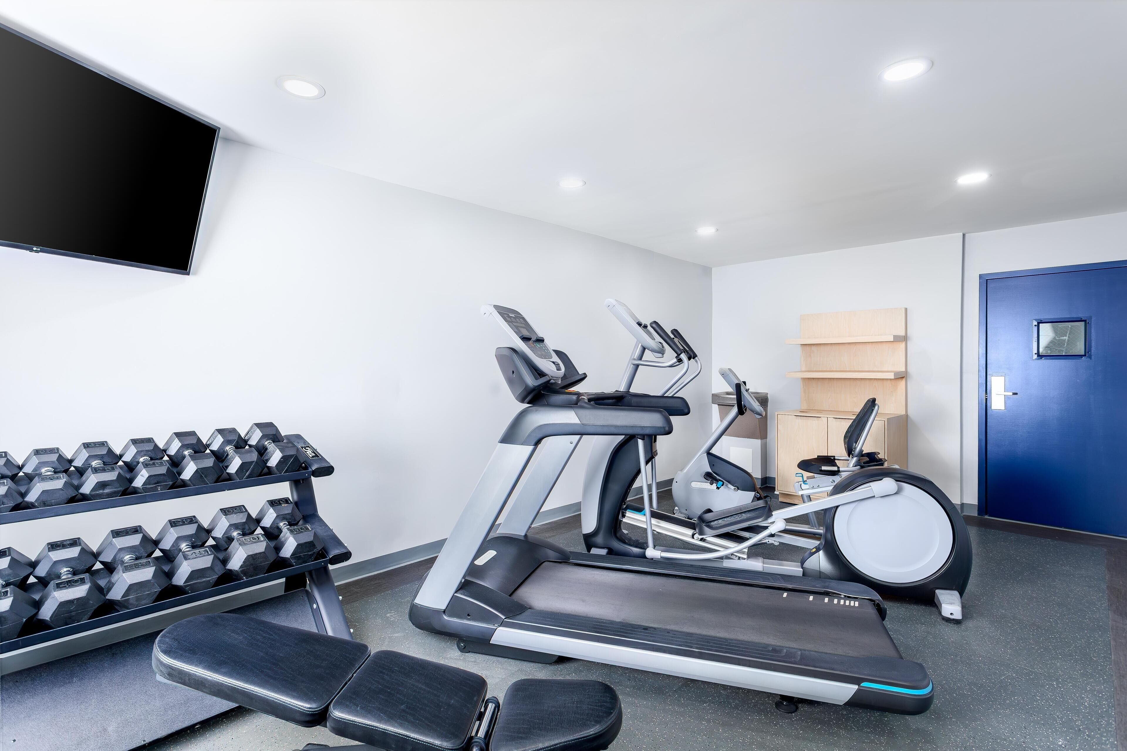 Un gimnasio con cintas de correr, mancuernas y bancos.