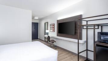 A hotel room with a bed, desk, chair, TV, and a minibar.