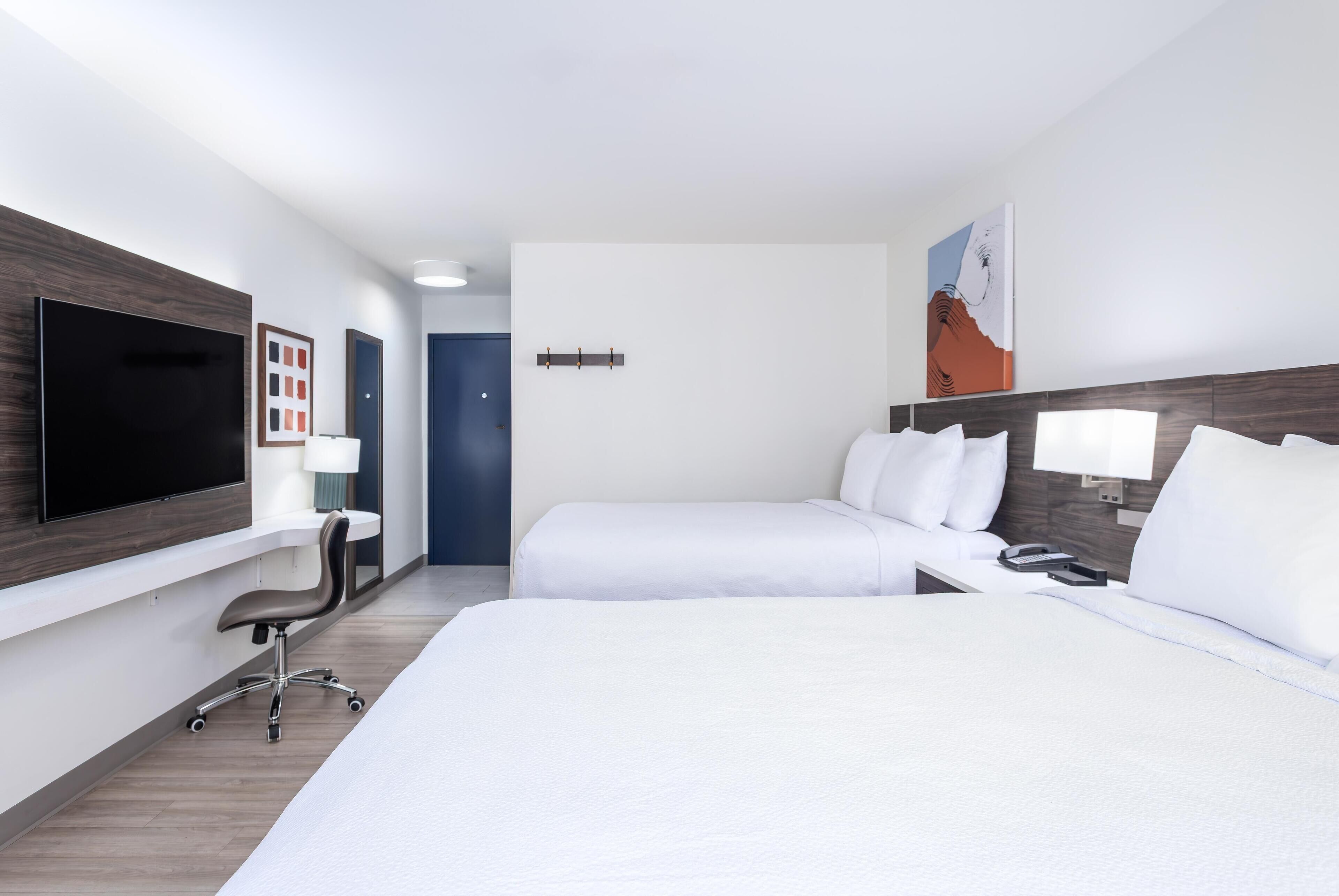 Habitación de hotel con dos camas, un escritorio, un televisor y un cuadro en la pared.