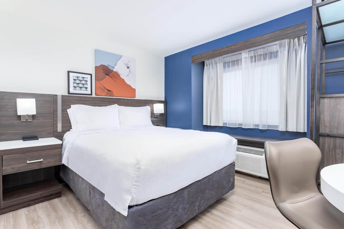 Una habitación de hotel moderna con una cama grande, una mesita de noche, una silla y una ventana con cortinas.