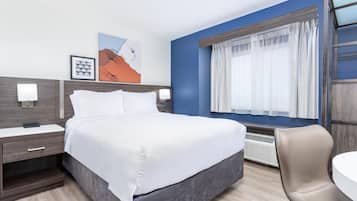 A modern hotel room with a large bed, a bedside table, a chair, and a window with curtains.