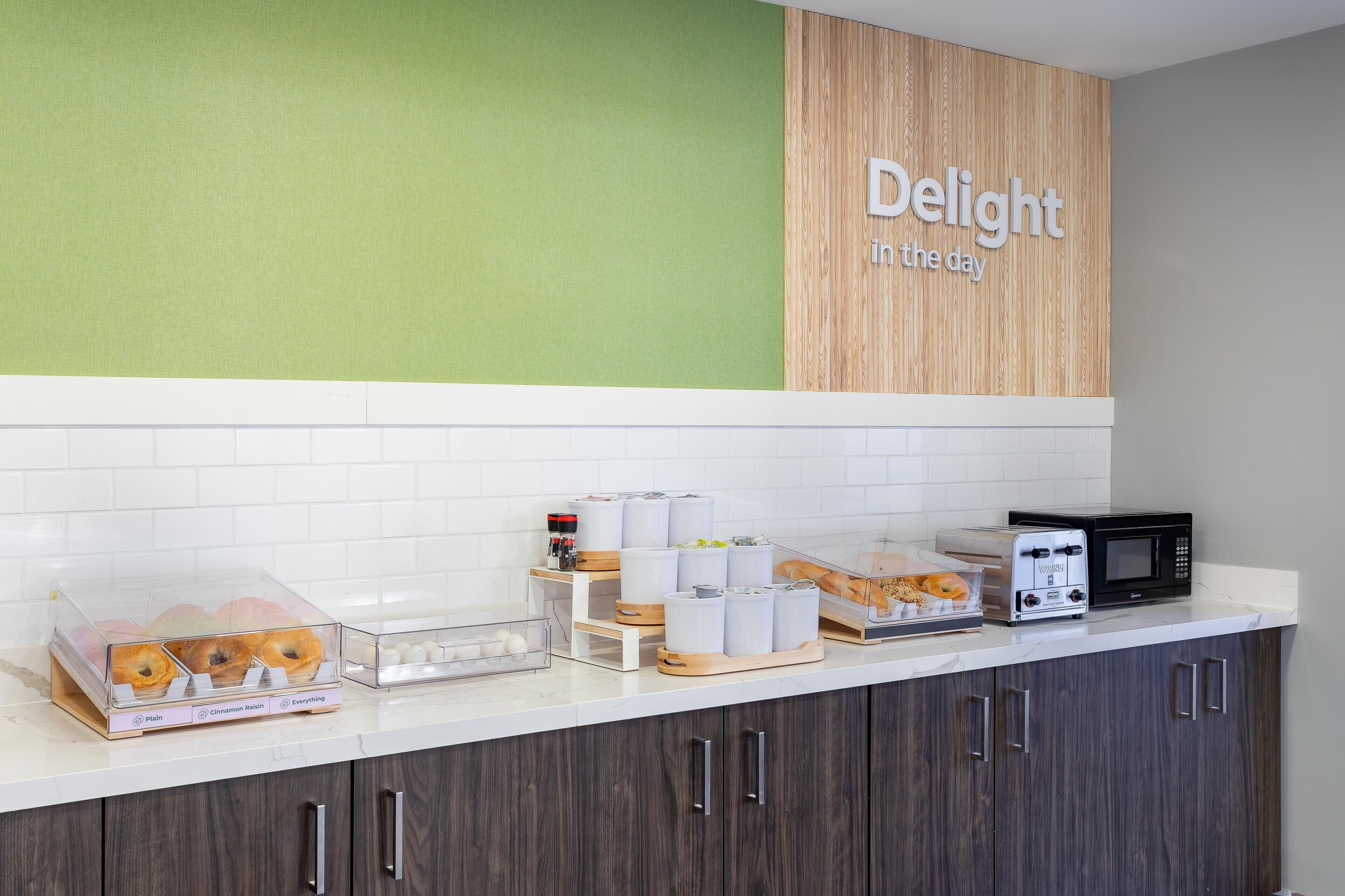 A kitchen counter with a deli display, including bagels and pastries, and a microwave oven.