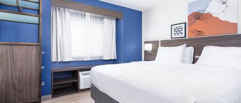 Una habitación de hotel con una cama grande, un escritorio con silla, un armario y una ventana con cortinas.