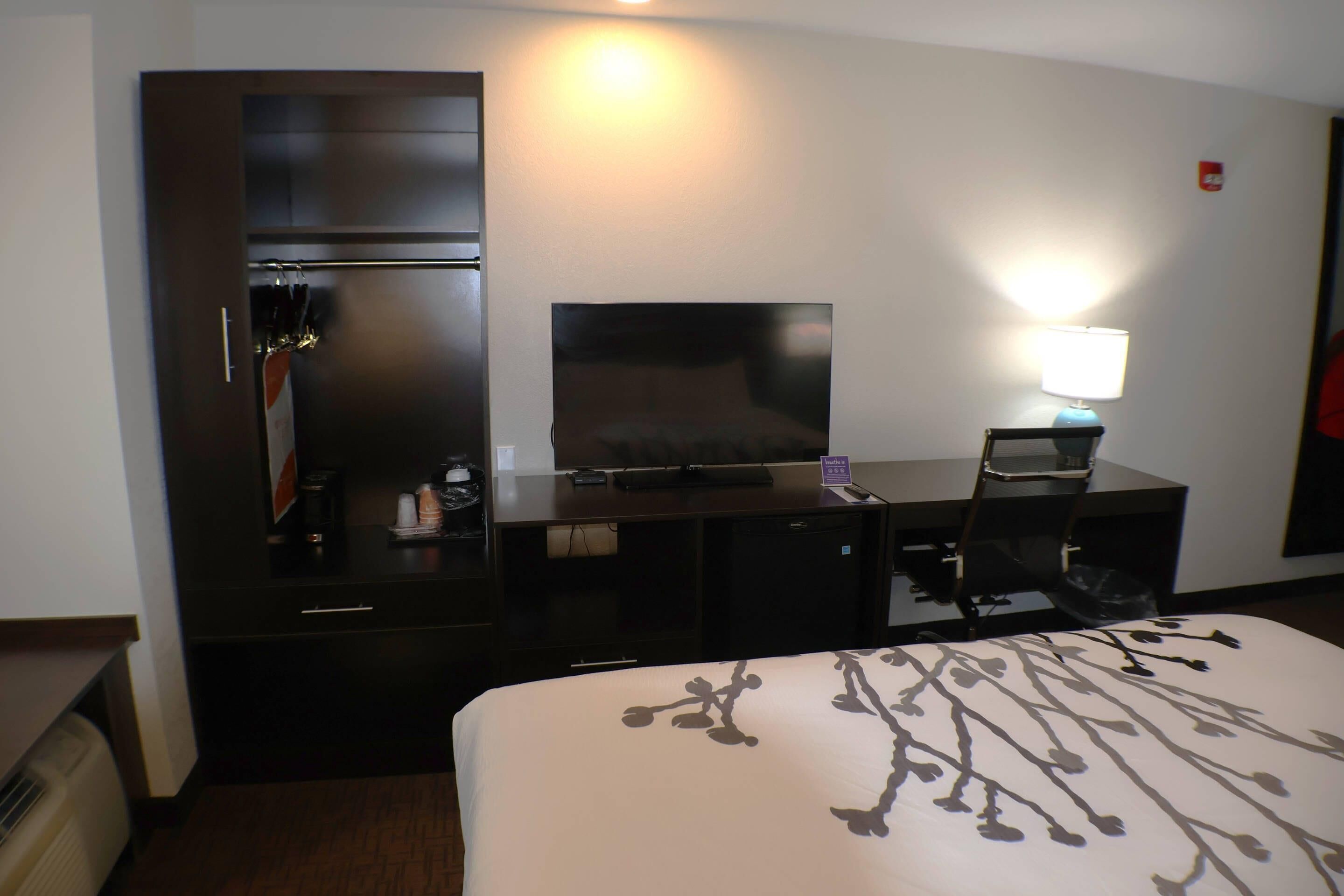 A hotel room with a bed, a desk with a computer, a television, a chair, and a lamp.