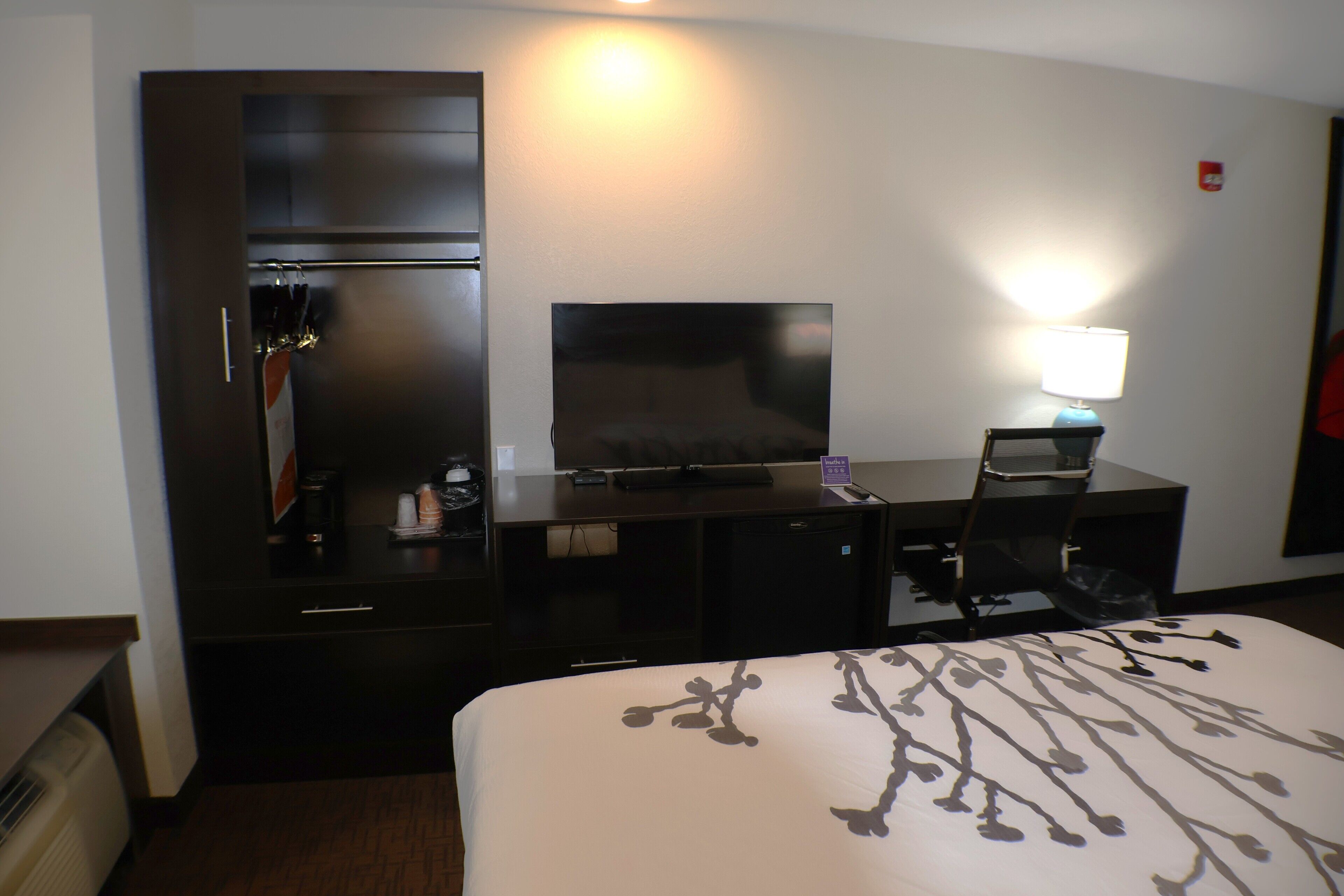 A hotel room with a bed, a desk with a computer, a TV, and a lamp.