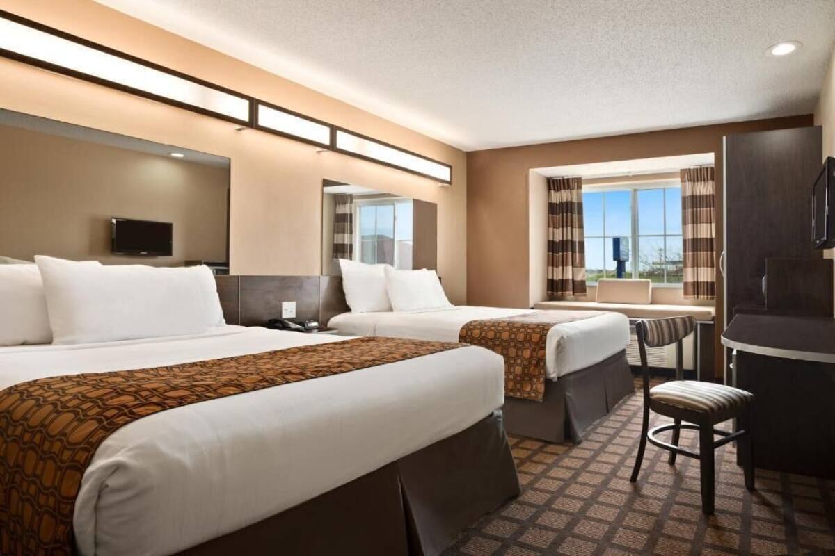 A hotel room with two beds, a desk, a chair, a television, and a large window with curtains.