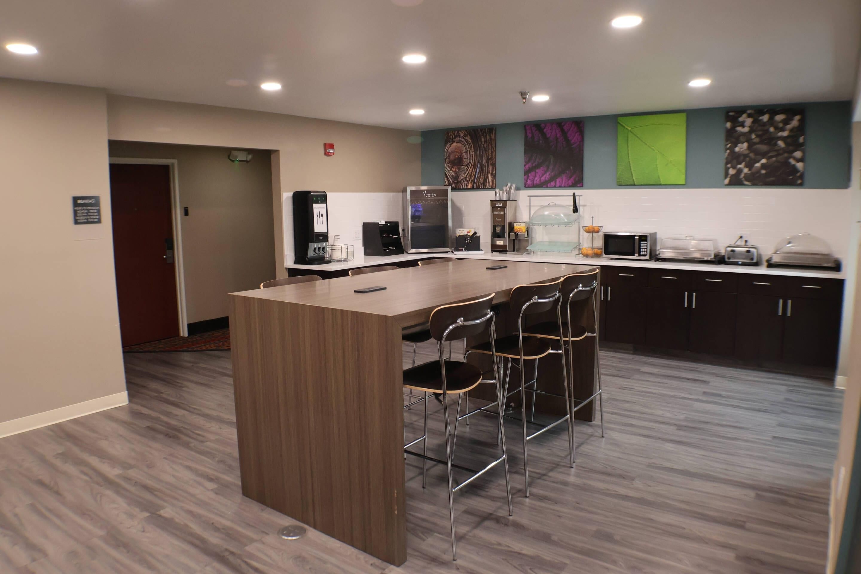 A modern kitchen with a central island, bar stools, a coffee station, and a microwave.