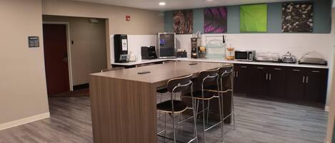 A modern kitchen with a central island, bar stools, a coffee station, and a microwave.