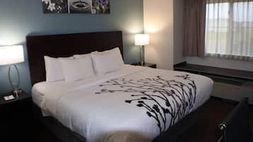 Cama bem arrumada com lençóis brancos e colcha florida preta, luminária de cabeceira, obra de arte na parede e janela com cortinas.