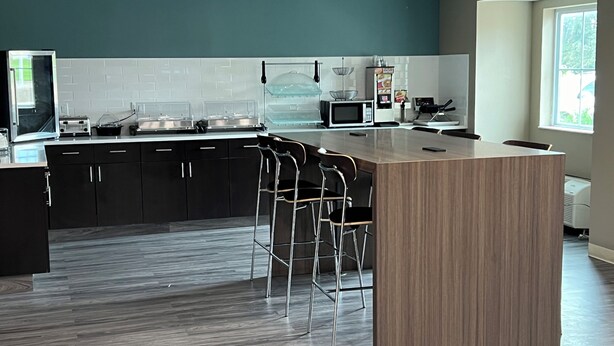 A modern kitchen with a central island, bar stools, black cabinets, and a microwave. - Sleep Inn Marion - Cedar Rapids (Marion)
