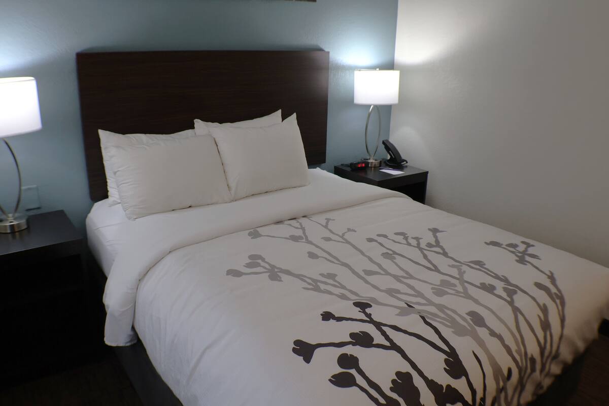 A neatly made bed with white linens and a floral pattern, a dark wooden headboard, and two bedside tables with lamps.