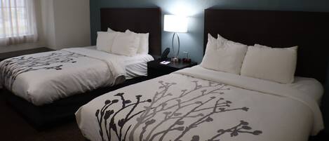 A hotel room with two beds, a nightstand, a lamp, and artwork on the walls.