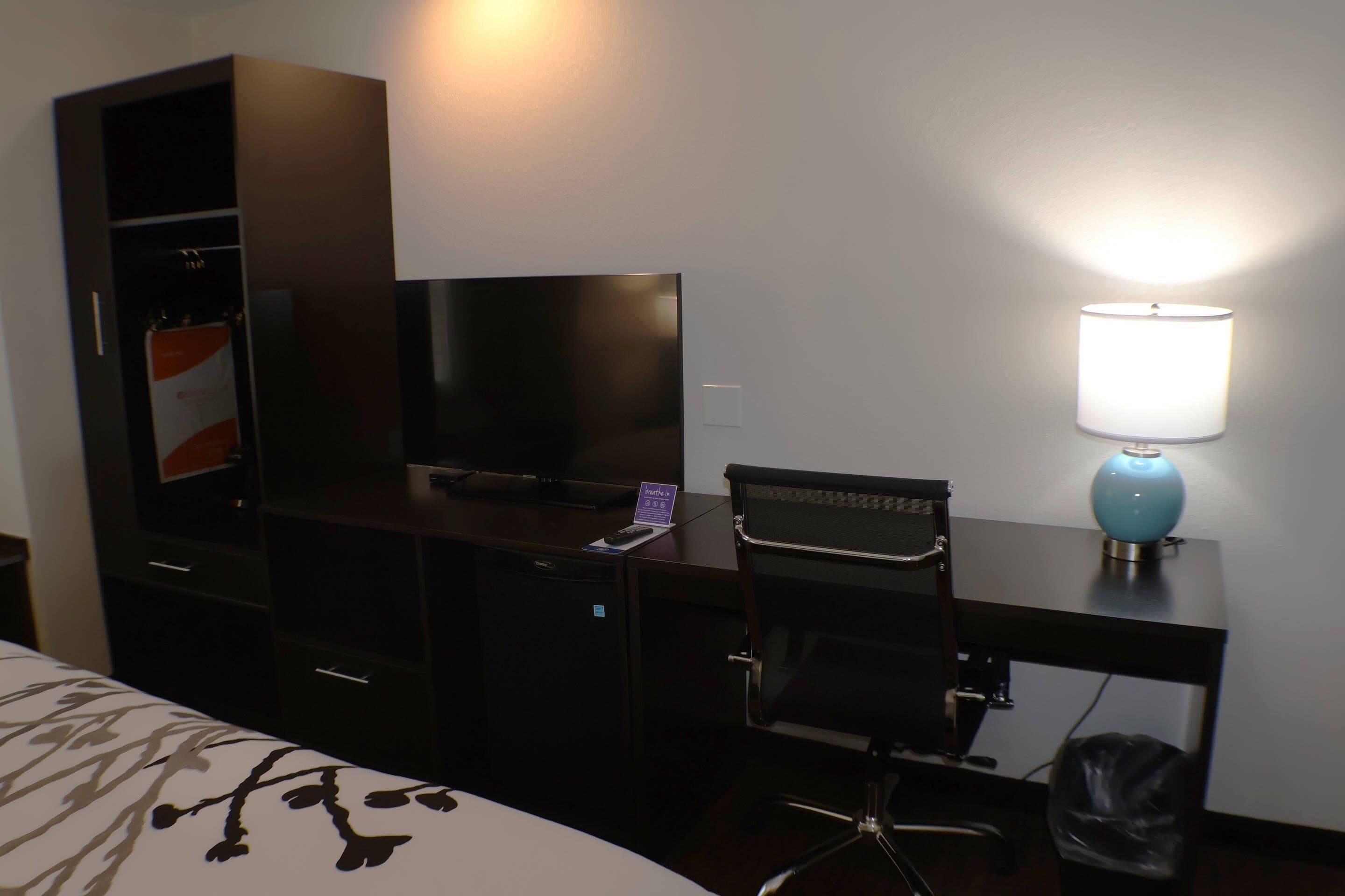 A hotel room with a bed, a desk with a computer, a TV, a lamp, and a wardrobe.