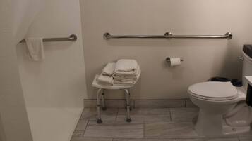 A bathroom with a toilet, a handrail, a towel rack, and a small stool.