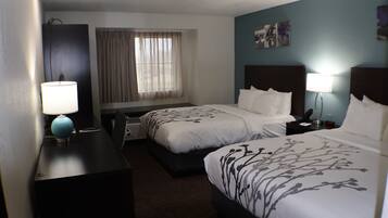 A hotel room with two beds, a desk, a lamp, and a window with curtains.
