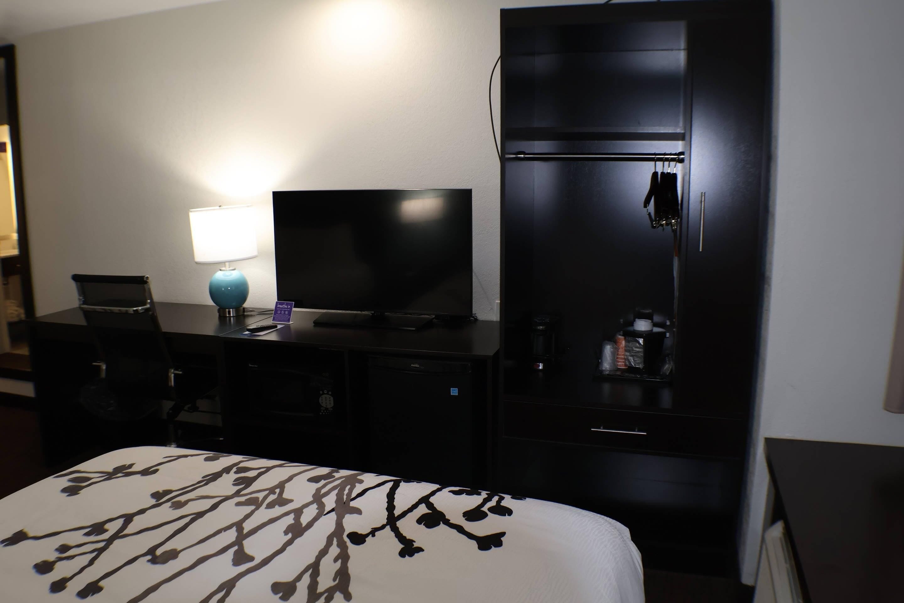 A hotel room with a bed, a desk with a computer, a television, a wardrobe, and a coffee machine.