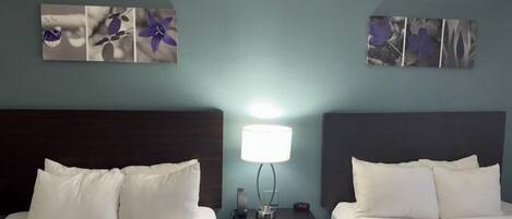 Habitación de hotel con dos camas, una mesita de noche con lámpara y decoración en la pared.