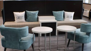 A modern seating area with a sofa and two round tables, each with a single chair. - Sleep Inn Marion - Cedar Rapids (Marion)