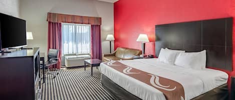 Habitación de hotel con una cama grande, un escritorio con televisor, una silla y una ventana con cortinas.