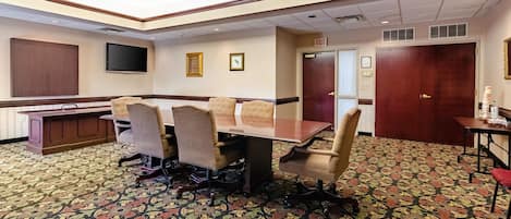 A conference room with a large table, four chairs, a television, and a patterned carpet.