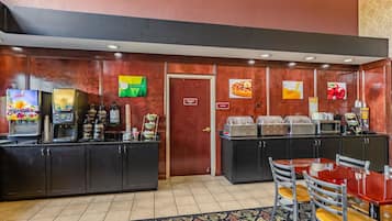 A hotel breakfast area with a coffee machine, juice dispenser, and food display.