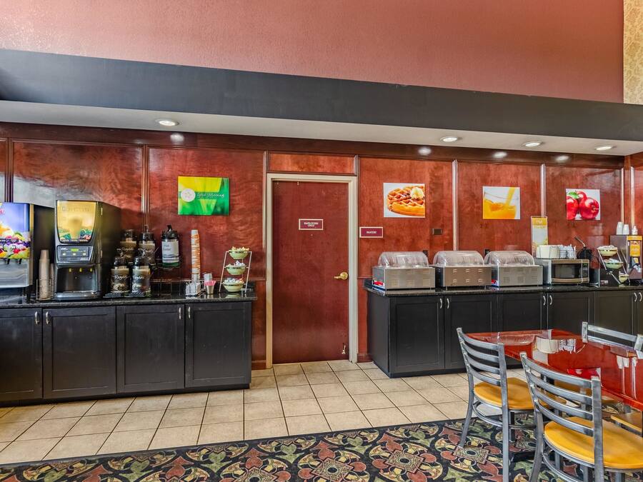 Zona de petit esmorzar d'hotel amb una màquina de cafè, un dispensador de suc i un expositor de menjar.