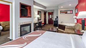 Hotelkamer met een groot bed, een open haard, een bureau met stoel, een bank, een badkuip en een televisie.