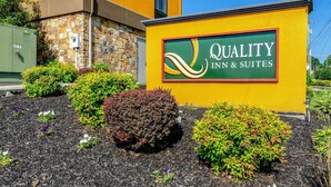 Een bordje voor Quality Inn & Suites met een gevel van steen en baksteen, omringd door aangelegde bloembedden en mulch.