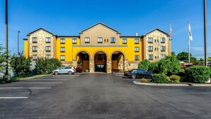 Een meerlaags hotel met een gele gevel, een grote entree met bogen, en een parkeerplaats met meerdere auto's.