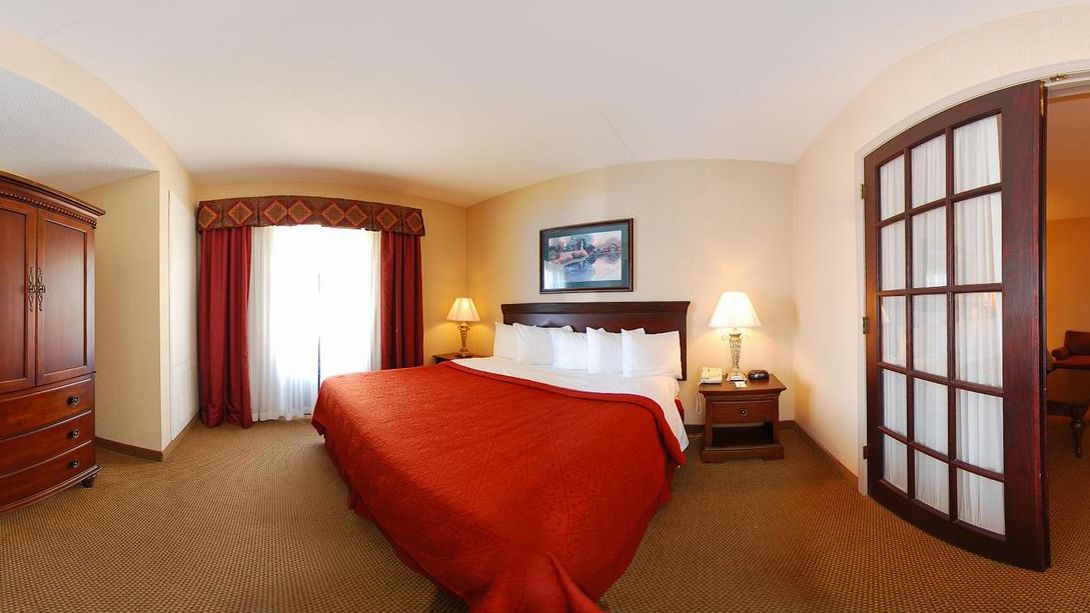 Une chambre d’hôtel avec un grand lit, deux tables de chevet avec des lampes, une armoire et une grande fenêtre avec des rideaux.