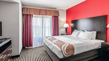 A hotel room with a large bed, a TV, a desk, and a window with curtains.