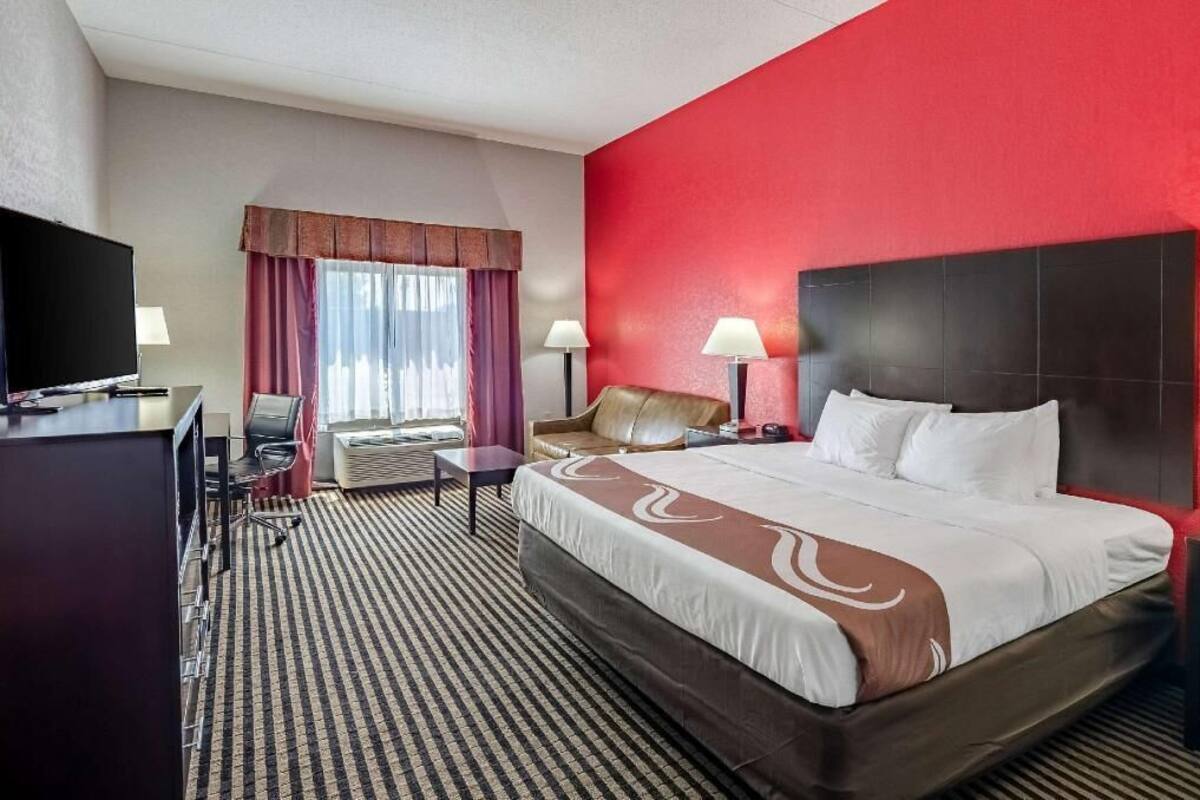 A hotel room with a large bed, a desk with a TV, a chair, and a window with curtains.