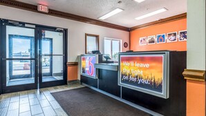 A hotel reception area with a glass door entrance, a reception desk, and a wall with framed pictures.