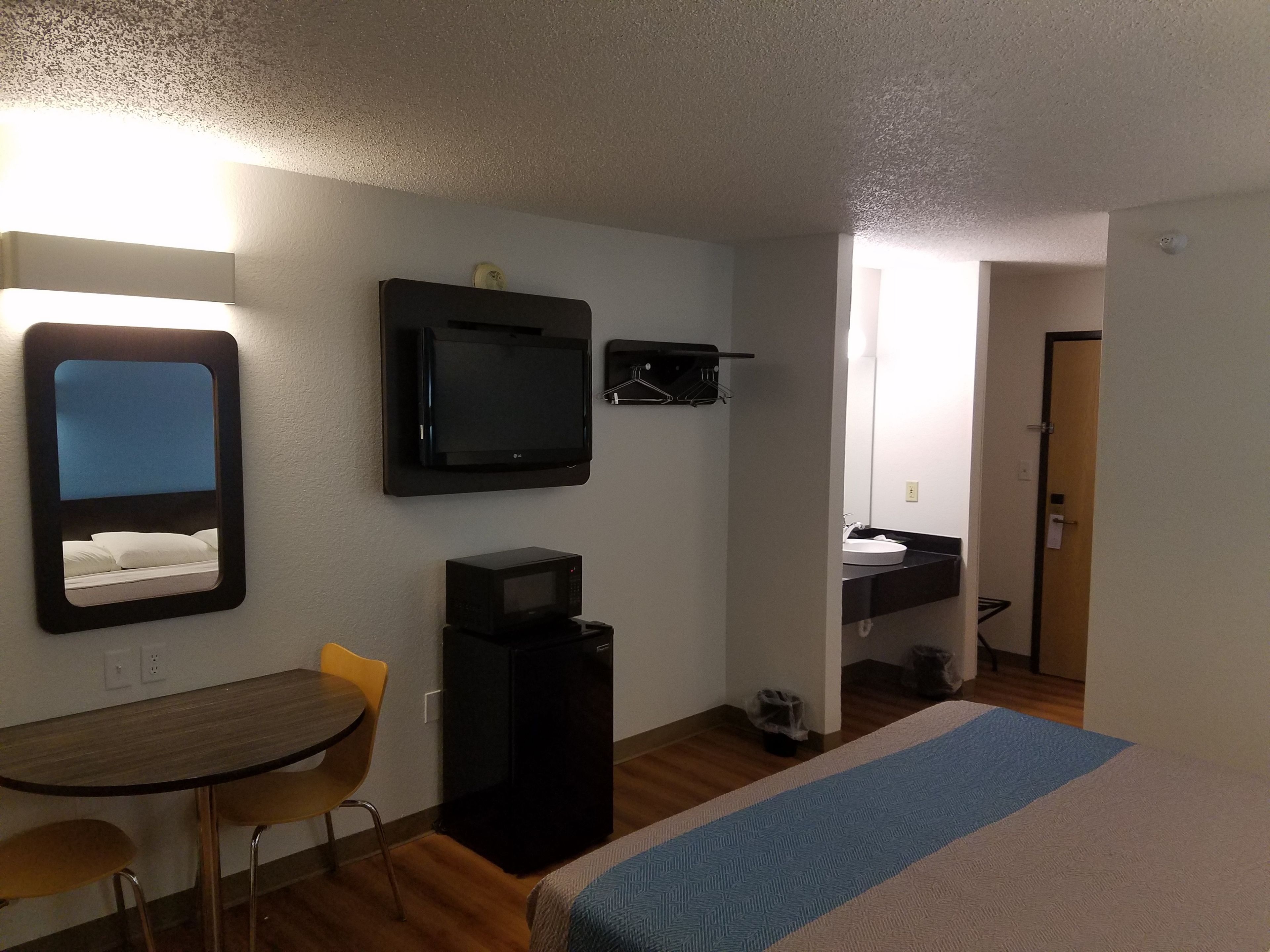 A hotel room with a bed, a desk, a chair, a TV, and a bathroom visible through an open door.