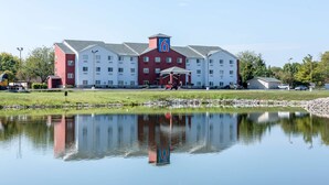 A large hotel with a prominent '6' logo, a pond in front, and a parking area with vehicles.